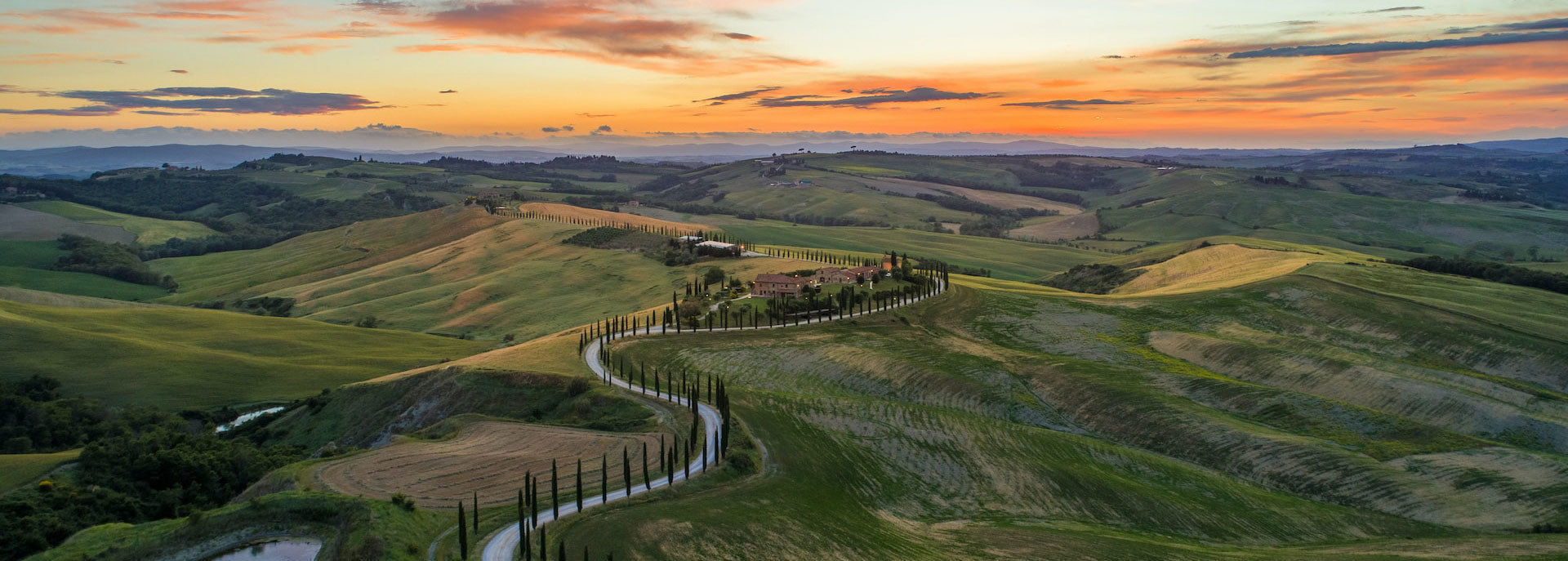 Paesaggio collinare al tramonto con cipressi e strada.